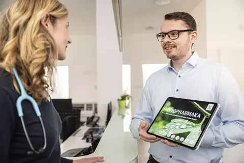 Ein Außendienstmitarbeiter spricht informiert eine Ärztin über pflanzliche Arzneimittel.