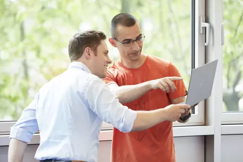 Ein IT-Mitarbeiter erklärt einem Kollegen etwas an einem Laptop