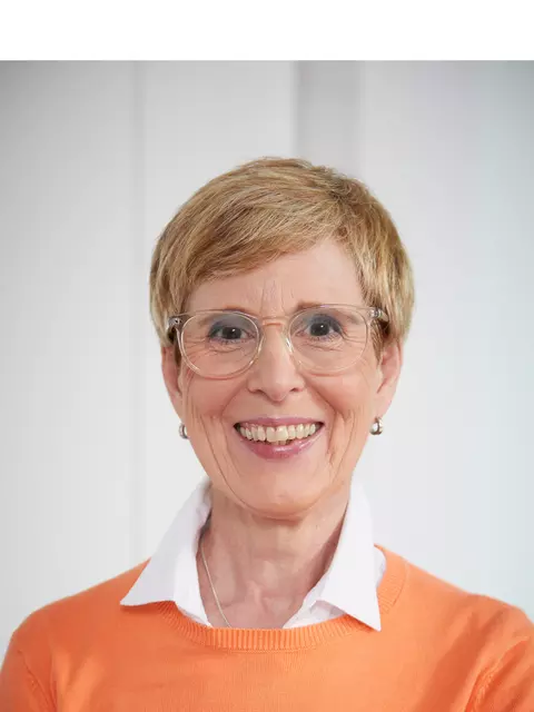 Frau mit Brille und orangenem Pullover lächelt in die Kamera