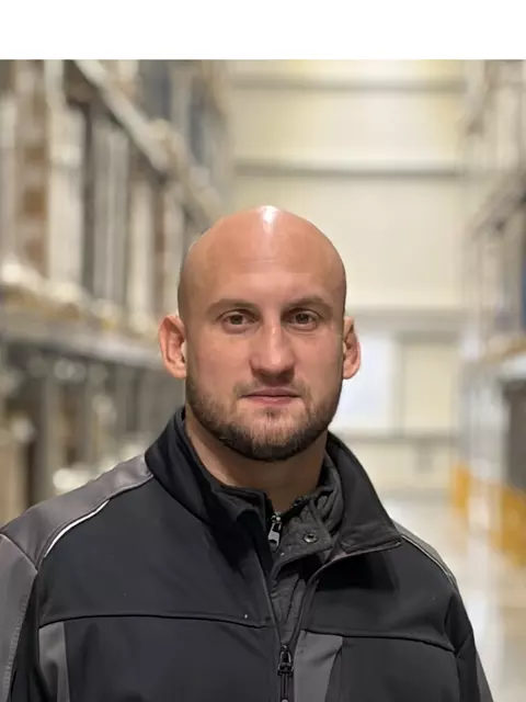 Ein Lagerarbeiter steht zwischen Regalen mit Paletten.