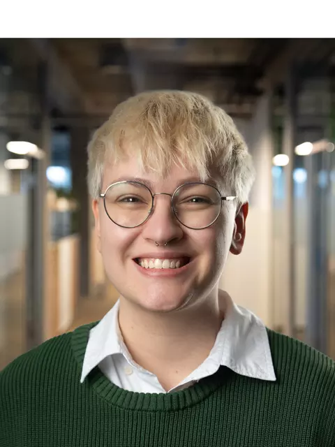 Eine Frau mit Brille und blonden Haaren steht im Flur eines Bürogebäudes.