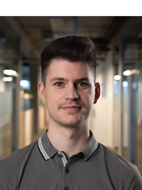 Ein Mann mit dunklen Haaren steht im Flur eines Bürogebäudes.